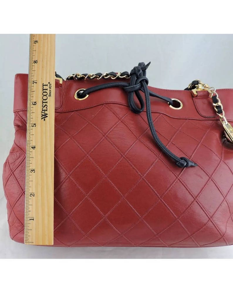 May include: A red quilted leather handbag with a black drawstring closure and a gold chain strap.