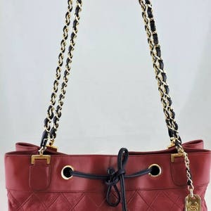May include: A red quilted leather handbag with a black and gold chain strap and a drawstring closure. The bag has a gold Chanel logo charm.
