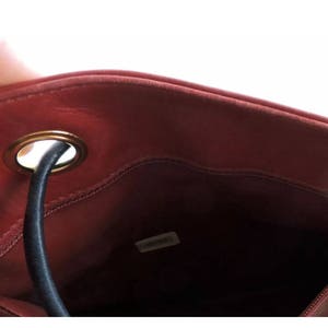May include: The inside of a red leather bag with a gold metal ring and a black drawstring. The bag has a small label inside that says "Chanel".