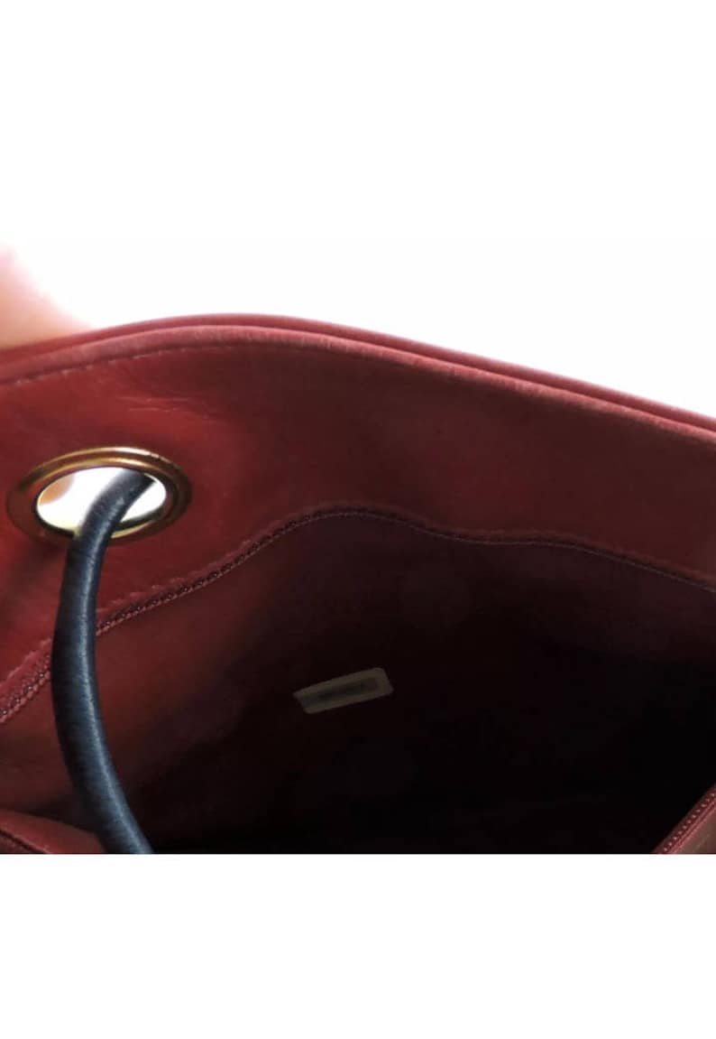 May include: The inside of a red leather bag with a gold metal ring and a black drawstring. The bag has a small label inside that says "Chanel".