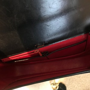 Pode incluir: O interior de uma bolsa de m&atilde;o de couro preto com forro vermelho. A bolsa tem fecho de correr e um fecho de metal dourado.