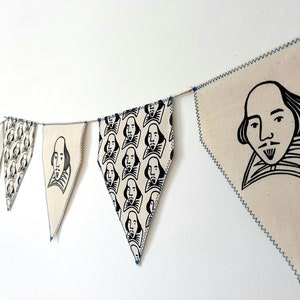 May include: A string of fabric bunting with a black and white illustration of William Shakespeare's face. The bunting is white with blue stitching and is strung together with twine.