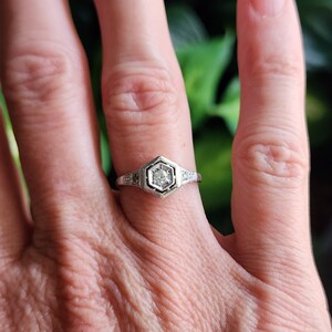 May include: A silver ring with a hexagonal setting featuring a single round diamond surrounded by smaller diamonds.
