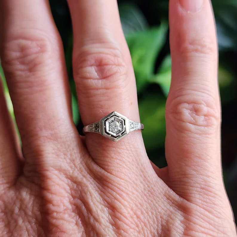 May include: A silver ring with a hexagonal setting featuring a single round diamond surrounded by smaller diamonds.