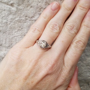 May include: A silver ring with a round, clear stone set in a filigree design.
