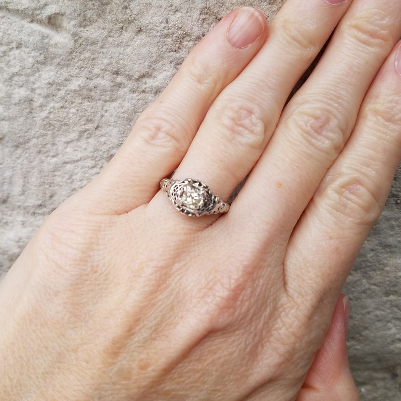 May include: A silver ring with a round, clear stone set in a filigree design.