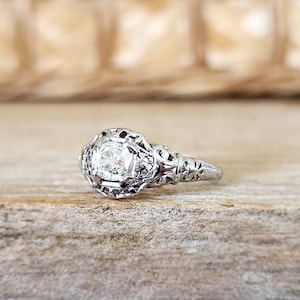 May include: A vintage silver engagement ring with a round, clear diamond set in a filigree design.