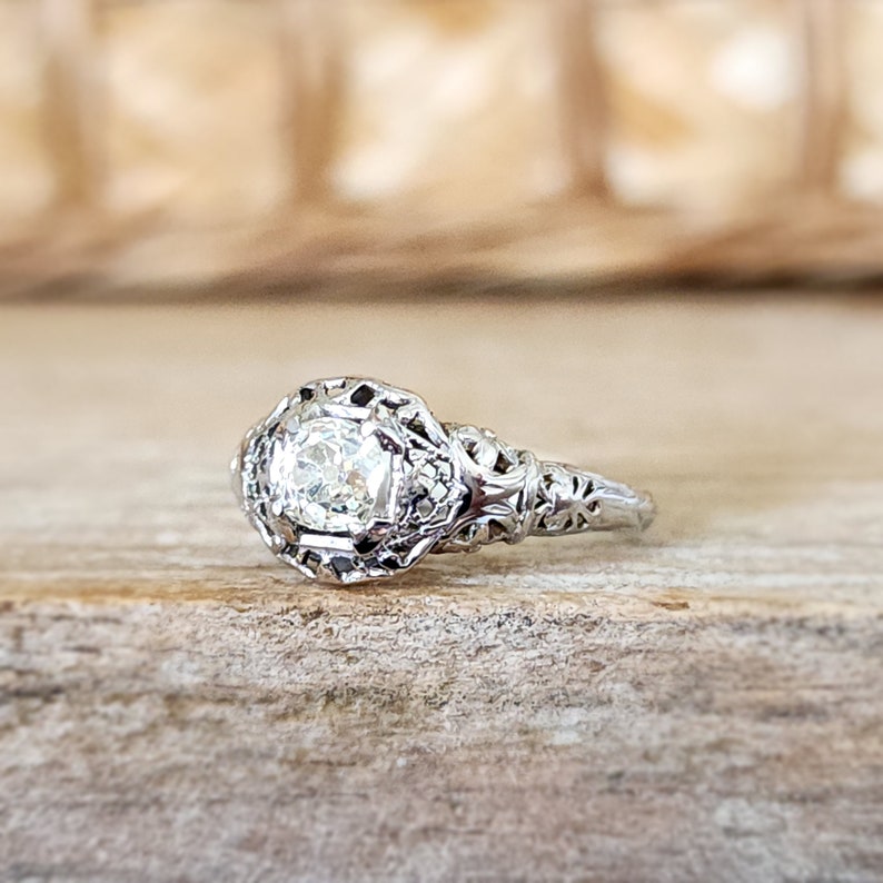 May include: A vintage silver engagement ring with a round, clear diamond set in a filigree design.