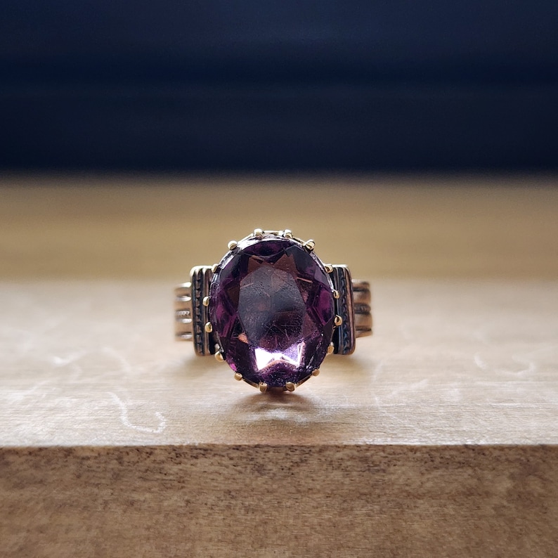 May include: A gold ring with a large, oval-shaped amethyst gemstone. The ring has a detailed, ornate setting.