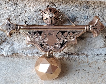 May include: A gold-toned pendant with a black enamel design and a dangling ball. The pendant has a geometric design and is attached to a chain.