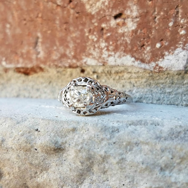 May include: A vintage engagement ring featuring a delicate filigree design and a round, clear centre stone.