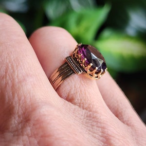 May include: A gold ring with a large, oval-shaped purple gemstone set in a decorative, ornate setting.