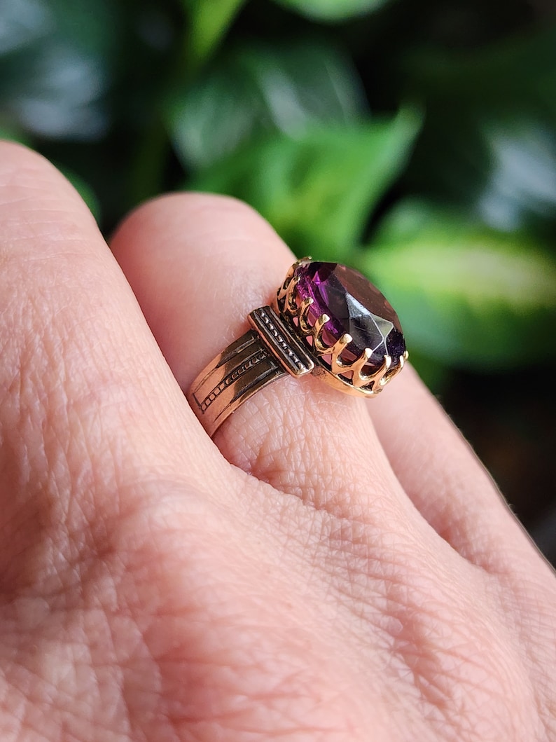 May include: A gold ring with a large, oval-shaped purple gemstone set in a decorative, ornate setting.