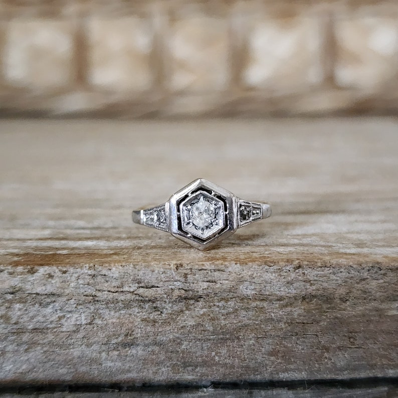 May include: A silver ring with a hexagonal setting featuring a single round diamond surrounded by smaller diamonds.