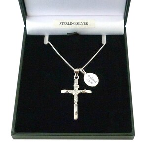 May include: A sterling silver crucifix pendant on a thin chain, presented in a black box. An oval charm attached to the chain is engraved with the text Confirmed 5.9.20. The box interior features a label with the text STERLING SILVER.