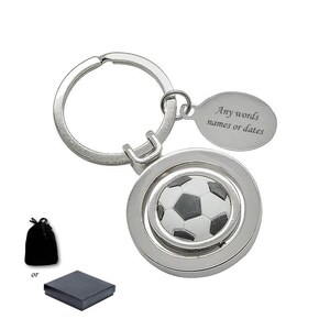 Peut inclure: Un porte-clés en métal argenté avec un médaillon circulaire orné d'un motif de ballon de football noir et blanc au centre. Il comporte une petite étiquette ovale gravée avec le texte Any words names or dates. Inclut une pochette ou boîte noire.
