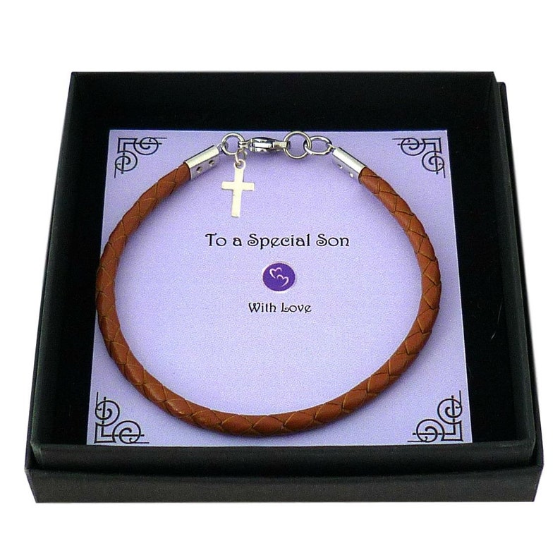 May include: A braided brown leather bracelet with a silver-toned cross charm and metal clasp, presented on a light purple card with the text To a Special Son and With Love, all contained within a black box.