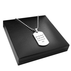 May include: A silver-coloured metal dog tag pendant necklace featuring a ball chain. The rectangular tag is engraved with the text: Best husband in the world love Lizzie xxx. The pendant is displayed on a black square box with a smooth finish.