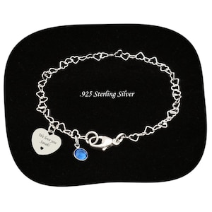 May include: A .925 sterling silver bracelet featuring a chain of small interconnected hearts. The bracelet includes a heart-shaped charm engraved with the text We love you Sarah! and a small blue circular gemstone charm with a lobster clasp.