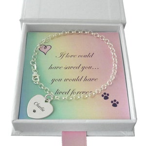 Peut inclure: Bracelet en argent avec un charme en forme de cœur gravé du nom "Charlie" et une empreinte de patte. Le bracelet est dans une boîte blanche avec un fond arc-en-ciel et le texte "Si l'amour avait pu te sauver... tu aurais vécu pour toujours".