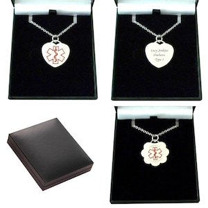 May include: Silver-toned medical alert necklaces with a red Star of Life symbol on heart-shaped and scalloped pendants. One pendant is engraved with the text Lucy Jenkins, Diabetes, Type 1. Each necklace is presented in a black display box.