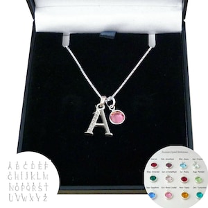 May include: A silver-toned necklace featuring a letter A pendant embellished with small clear stones and a separate round pink crystal charm. The jewellery is presented in a black box, accompanied by a chart showing alphabet letter options and a guide to twelve different coloured Austrian crystal birthstones.