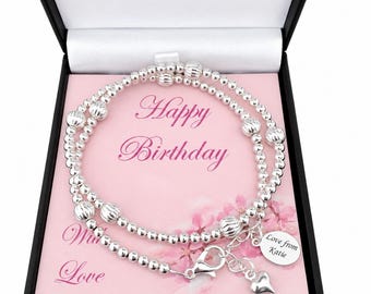 May include: A silver beaded bracelet with textured spherical beads and a small round charm engraved with the text Love from Katie, presented in a black box with a pink card featuring the text Happy Birthday and With Love.