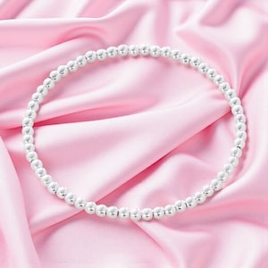 Peut inclure: Un collier circulaire composé de petites perles sphériques uniformes et polies de couleur argentée, disposées en une boucle continue. La surface métallique des perles reflète la lumière, créant un aspect brillant sur tout le brin.