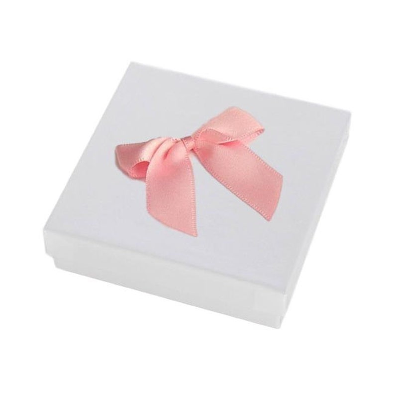 May include: A square white gift box featuring a smooth matte finish, topped with a single decorative light pink satin ribbon bow centered on the lid. The box has clean, sharp edges and a simple, structured design for holding small items.