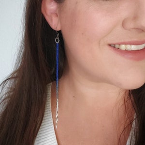 Puede incluir: Un par de pendientes largos de cuentas plateadas y azules. Los pendientes son colgantes y tienen un gancho plateado.