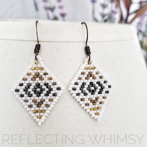 May include: A pair of white, black, and gold beaded earrings with a diamond shape. The earrings have a simple, geometric design.