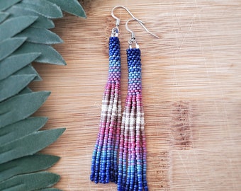 May include: A pair of long, beaded earrings with a gradient of blue, pink, and white colors. The earrings are made with small, round beads and have silver hooks.