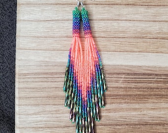 Pendientes largos con borlas degradadas de cuentas de semillas en color naranja neón arcoíris y estilo caprichoso.