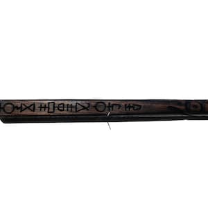 May include: A dark brown wooden wand with black carved symbols and designs. The wand is approximately 30 cm long.