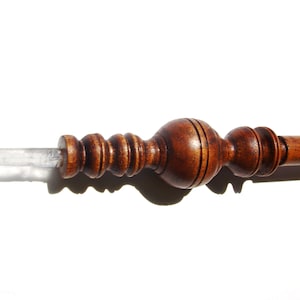 May include: A wooden wand with a clear quartz crystal tip. The wand has a brown wood finish and intricate carvings.