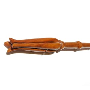 May include: A wooden wand with a carved flower design at the top. The wand is brown and has a smooth finish.