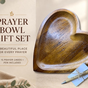 May include: A heart-shaped wooden bowl with three engraved crosses, accompanied by a pen and prayer cards. The text reads: PRAYER BOWL GIFT SET, A BEAUTIFUL PLACE FOR EVERY PRAYER, 15 PRAYER CARDS + PEN INCLUDED, and the pen says Pray Without Ceasing.