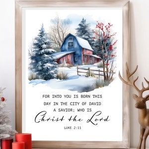 May include: Framed watercolor print featuring a winter scene with a red and blue barn, snow-covered trees, and the text "Christ the Lord" from Luke 2:11. The artwork is set in a light wooden frame, suitable for home decor.