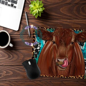 May include: A brown cow with a pink tongue sticking out, on a blue and brown animal print background. The cow is looking directly at the camera.