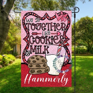 May include: A pink and red garden flag with a white polka dot background. The flag features a heart design with the text "We go together like cookies & milk" and the name "Hammerly".