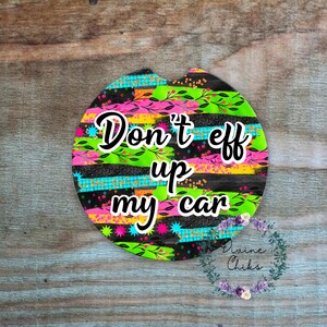 May include: A round car air freshener with a black, green, pink, and yellow striped background. The text "Don't eff up my car" is written in white on the air freshener.