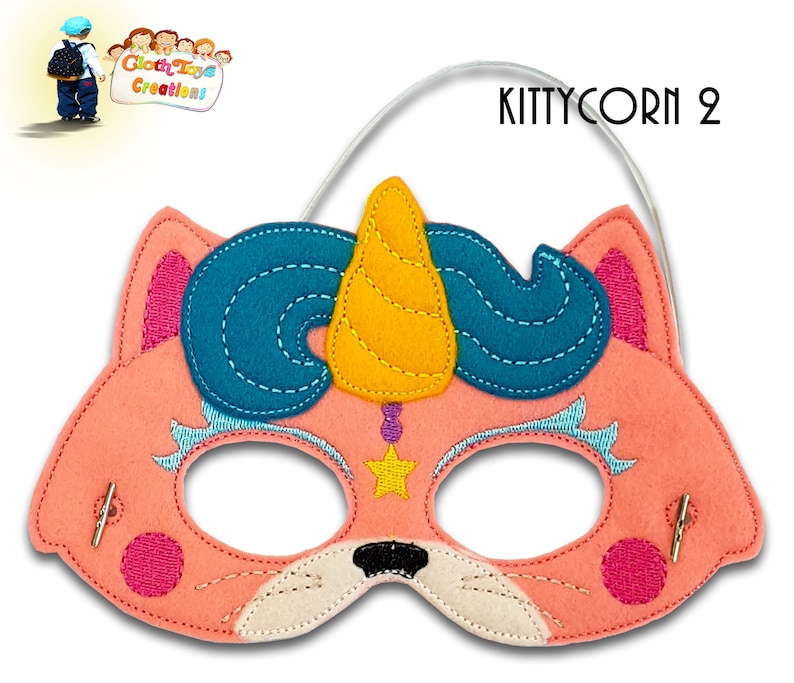 May include: Pink felt cat mask with a blue and yellow unicorn horn, a star, and pink accents. The mask has elastic straps for wearing. "KITTYCORN 2" is written in the top right corner.