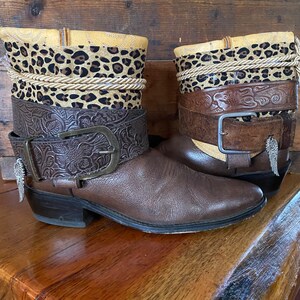 May include: A pair of brown leather cowboy boots with a leopard print fabric lining and a brown leather belt with a buckle. The boots have a pointed toe and a low heel.