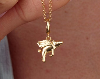 May include: A gold-toned necklace featuring a small, three-dimensional pendant shaped like a flying pig with detailed wings. The pendant hangs from a delicate, thin gold-toned chain, showcasing a polished, reflective metallic finish throughout.
