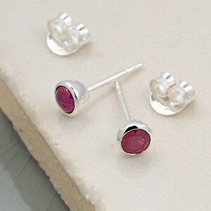 May include: A pair of silver stud earrings with small, round, red gemstones.