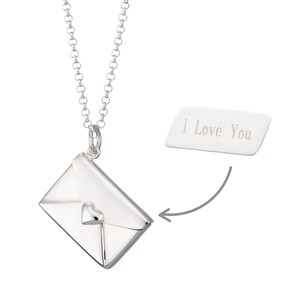 May include: A silver-colored necklace with a pendant shaped like an envelope with a heart detail. The necklace has a chain with round links. A white rectangular tag with the text "I Love You" is next to the pendant.