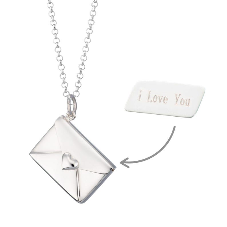 May include: A silver-colored necklace with a pendant shaped like an envelope with a heart detail. The necklace has a chain with round links. A white rectangular tag with the text "I Love You" is next to the pendant.