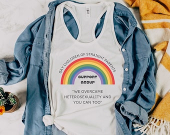 May include: White tank top with a rainbow graphic and the text "GAY CHILDREN OF STRAIGHT PARENTS SUPPORT GROUP". The tank top is paired with a blue denim shirt and a yellow and white blanket.