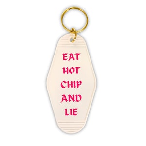 May include: White motel key chain with a gold key ring. The key chain has pink text that reads "EAT HOT CHIP AND LIE."