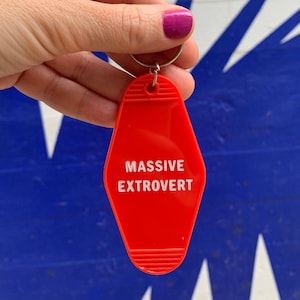 May include: Red motel key chain with the text "MASSIVE EXTROVERT" in white lettering.